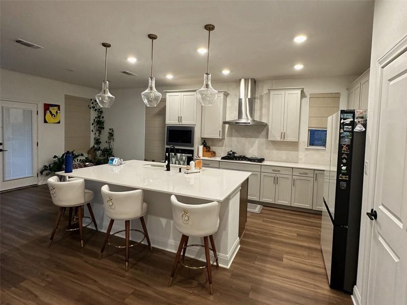 Modern kitchen featuring a large central island with seating, white shaker cabinetry, stainless steel appliances, and wood-finish flooring Modern kitchen featuring a large central island with seating, white shaker cabinetry, stainless steel appliances, and wood-finish flooring