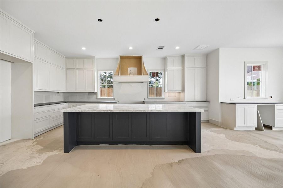 Chef’s kitchen with a symmetrical design anchored by a statement vent hood and flanked by double windows for natural light. Floor to ceiling cabinetry provides exceptional storage, while the oversized island offers generous workspace and seating. Clean lines, bright finishes, and a functional layout combine to create a highly efficient and visually striking culinary space.