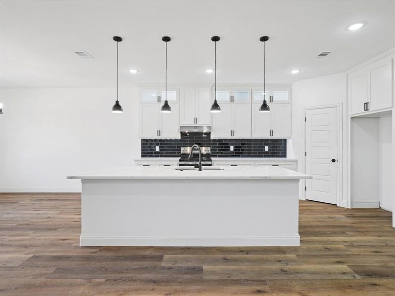 Kitchen featuring hanging light fixtures, a kitchen island with sink, dark wood-type flooring, white cabinets, and light stone counters