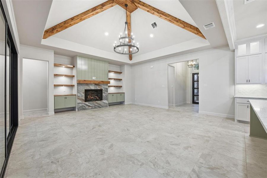 Unfurnished living room featuring a chandelier, a high end fireplace, built in shelves, a tray ceiling, and recessed lighting Unfurnished living room featuring a chandelier, a high end fireplace, built in shelves, a tray ceiling, and recessed lighting