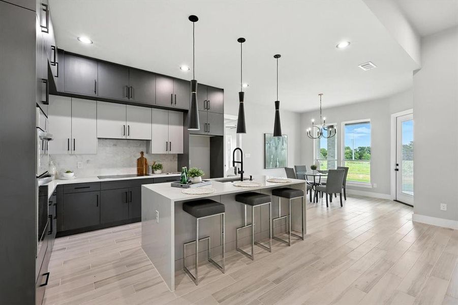Kitchen with black electric cooktop, a chandelier, a kitchen island with sink, backsplash, and light countertops Kitchen with black electric cooktop, a chandelier, a kitchen island with sink, backsplash, and light countertops