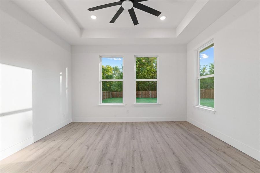 Spare room with ceiling fan, a raised ceiling, and light hardwood / wood-style flooring