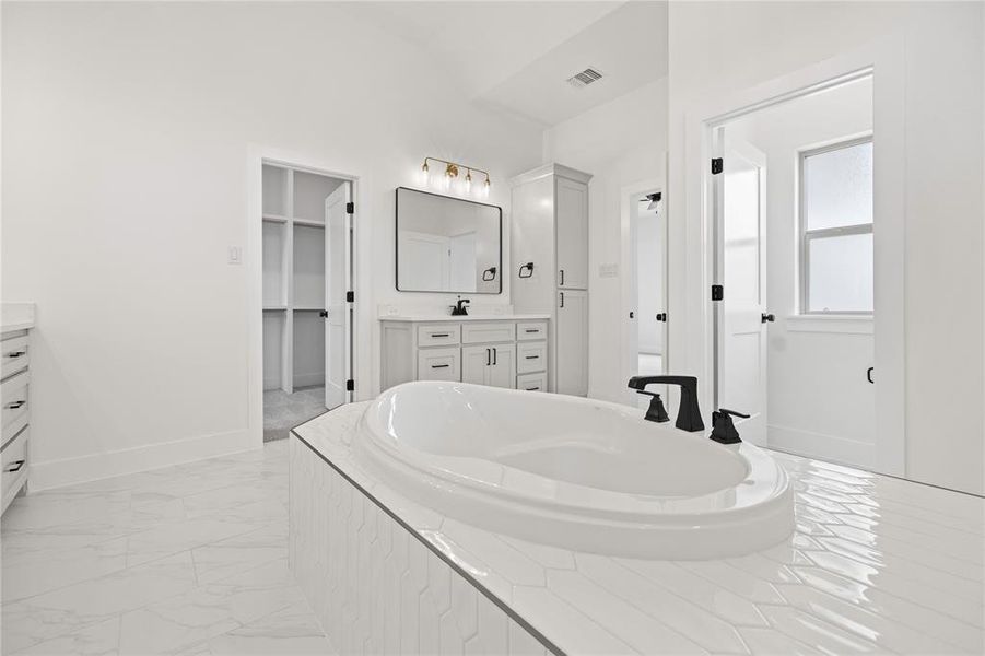 Full bathroom featuring vanity, a garden tub, light marble finish floors, and a walk in closet Full bathroom featuring vanity, a garden tub, light marble finish floors, and a walk in closet