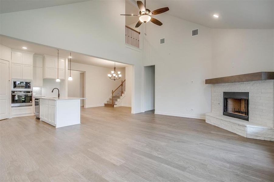 Unfurnished living room with ceiling fan with notable chandelier, a fireplace, high vaulted ceiling, and light hardwood / wood-style floors