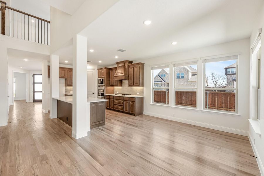 Open living area with light wood floors leading to kitchen with brown cabinets and white countertops