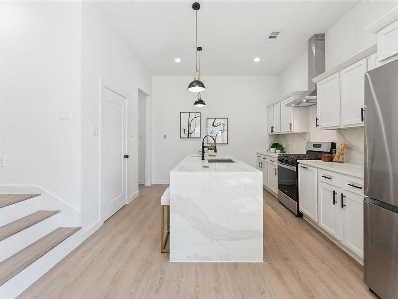 Kitchen with a kitchen island with sink, a sink, white cabinets, appliances with stainless steel finishes, and pendant lighting