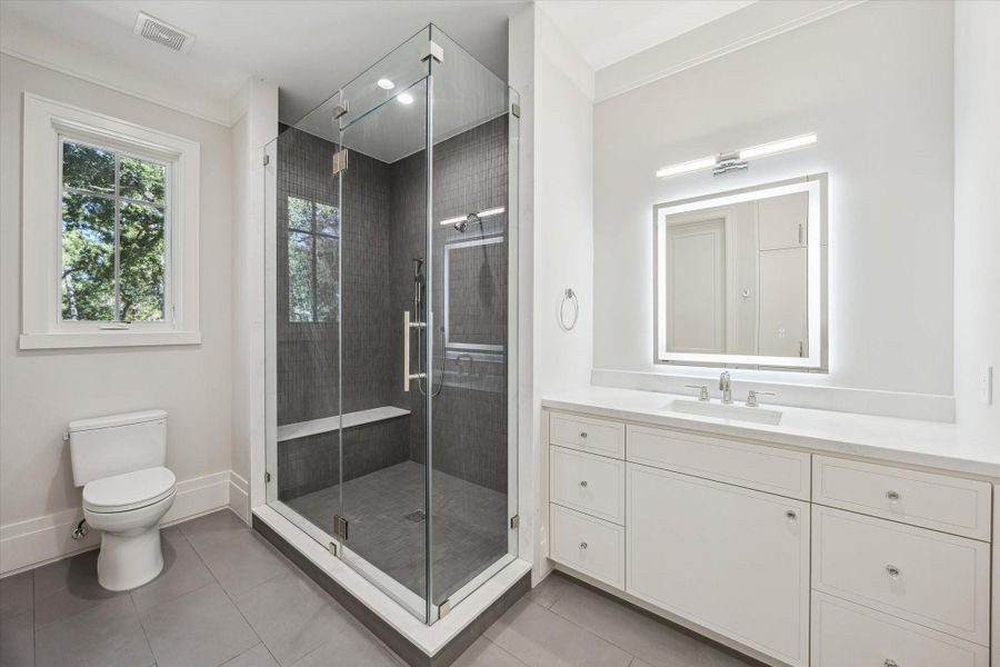 One of four en-suite baths, featuring a walk-in shower with frameless glass enclosure, custom cabinetry, and mirror lighting that creates a refined, tailored finish.