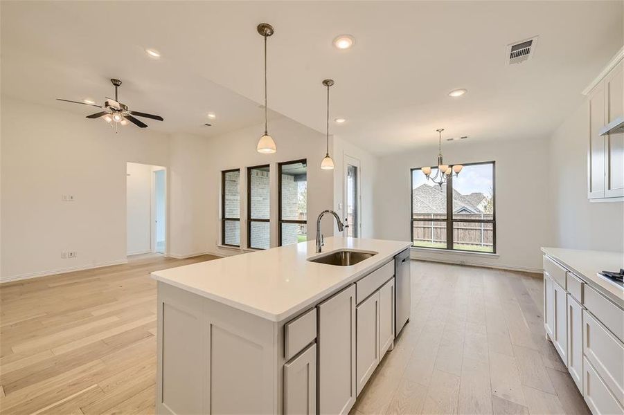 Kitchen featuring hanging light fixtures, stainless steel dishwasher, an island with sink, light hardwood / wood-style flooring, and sink