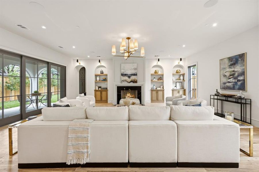 Spacious living area featuring light wood-finish flooring, a fireplace with a dark surround, and built-in arched shelving with lower cabinetry Spacious living area featuring light wood-finish flooring, a fireplace with a dark surround, and built-in arched shelving with lower cabinetry