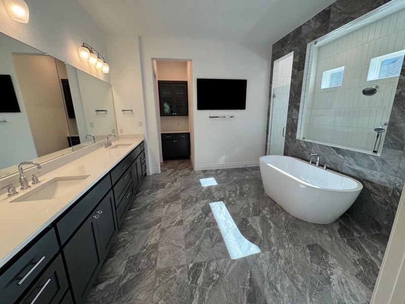 Bathroom with a freestanding tub, double vanity, tiled shower, and dark marble finish floors