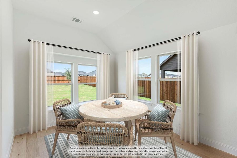 Breakfast nook with round wood table, woven chairs, vaulted ceiling, and large windows overlooking backyard