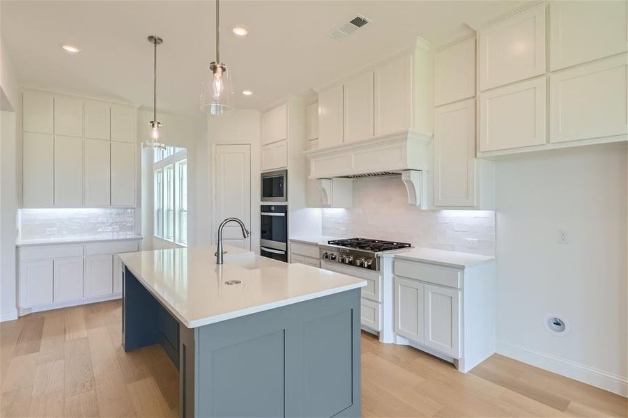 Kitchen with appliances with stainless steel finishes, backsplash, a center island with sink, and light hardwood / wood-style flooring