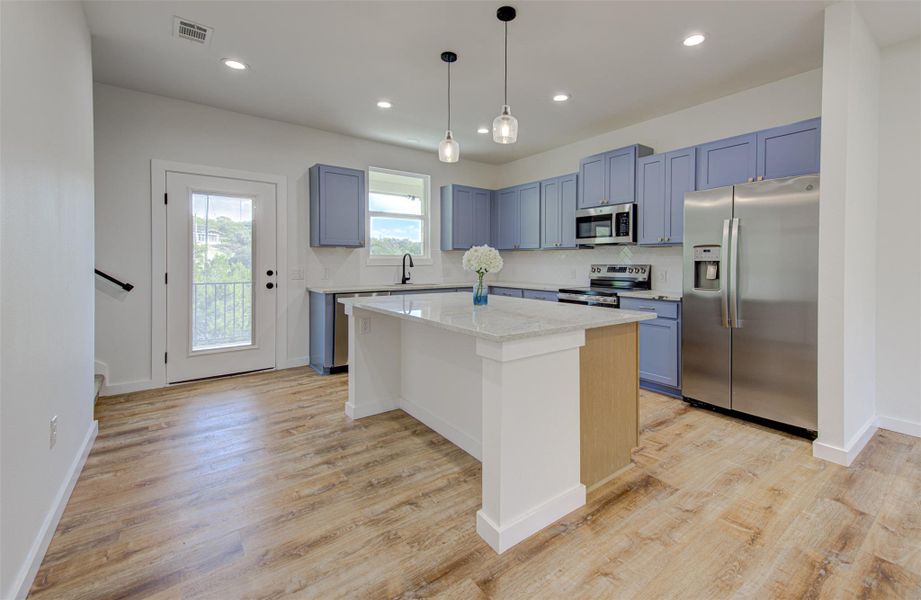 Kitchen with stainless steel appliances, a center island, pendant lighting, light stone counters, and recessed lighting