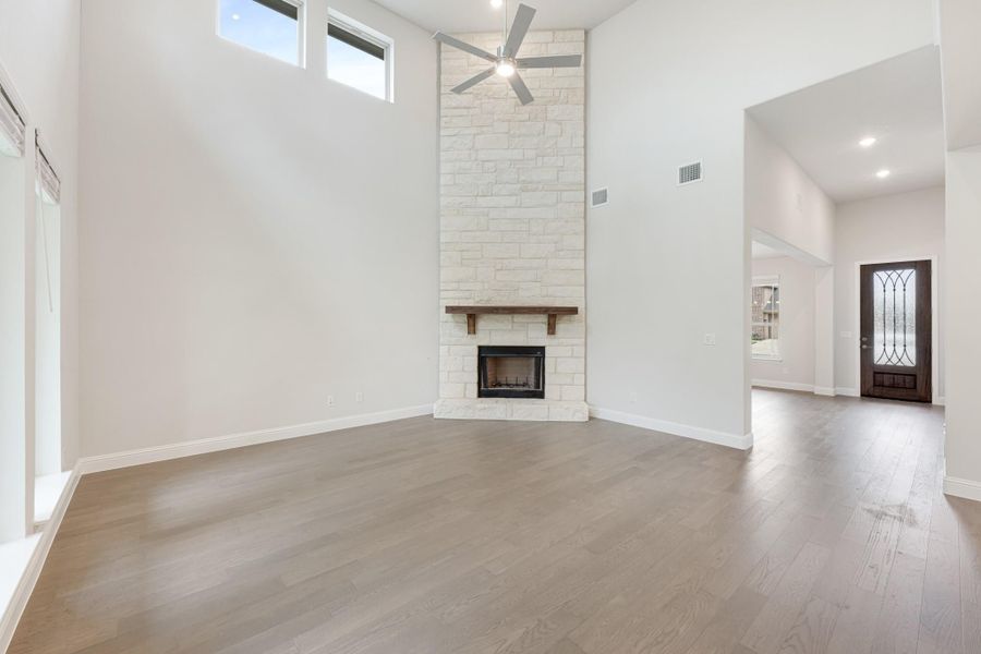 Open living room with tall stone fireplace, ceiling fan, hardwood floors, and view to front entry door Open living room with tall stone fireplace, ceiling fan, hardwood floors, and view to front entry door