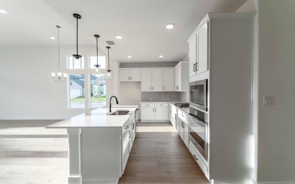 Kitchen with stainless steel appliances, light wood-style flooring, decorative light fixtures, white cabinetry, and a center island with sink