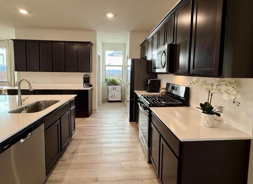 Kitchen with appliances with stainless steel finishes, decorative backsplash, light wood finished floors, light stone counters, and recessed lighting