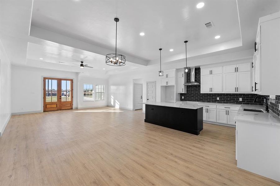Kitchen featuring open floor plan, a raised ceiling, a kitchen island, white cabinets, and recessed lighting