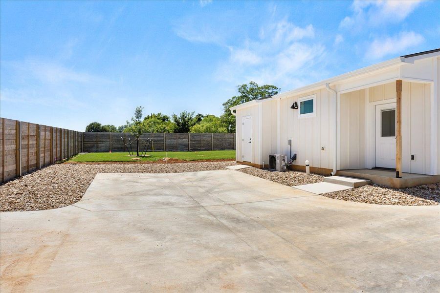 A well-maintained concrete driveway leads to a pristine side entrance, complemented by a neatly fenced yard.