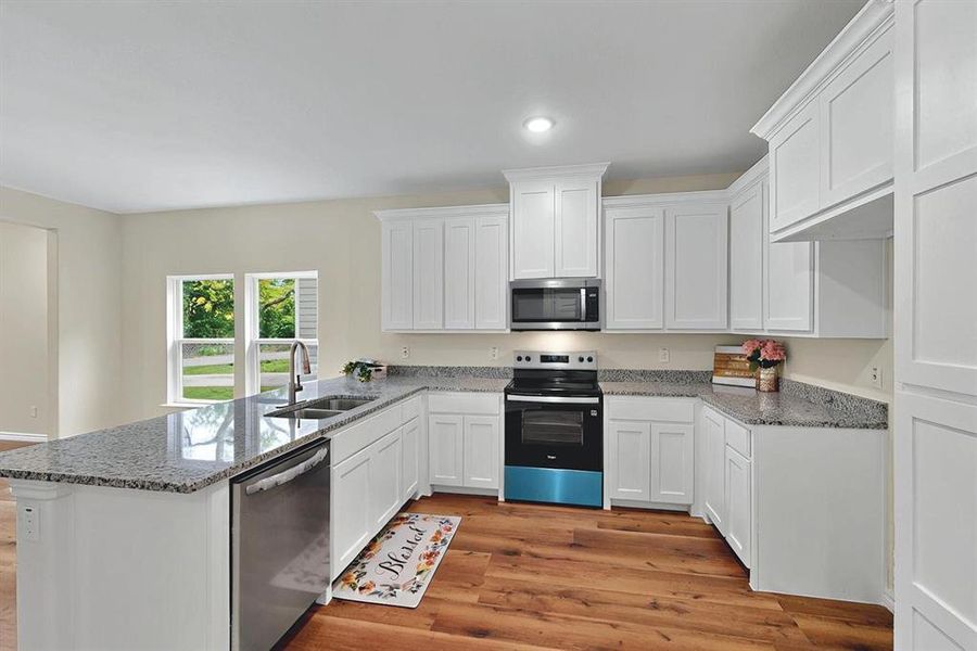 Kitchen featuring a peninsula, white cabinetry, a sink, light wood-style flooring, and appliances with stainless steel finishes Kitchen featuring a peninsula, white cabinetry, a sink, light wood-style flooring, and appliances with stainless steel finishes