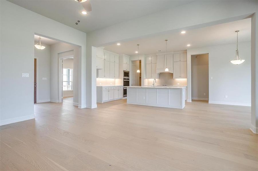 Kitchen with hanging light fixtures, white cabinets, light hardwood / wood-style floors, sink, and a center island with sink