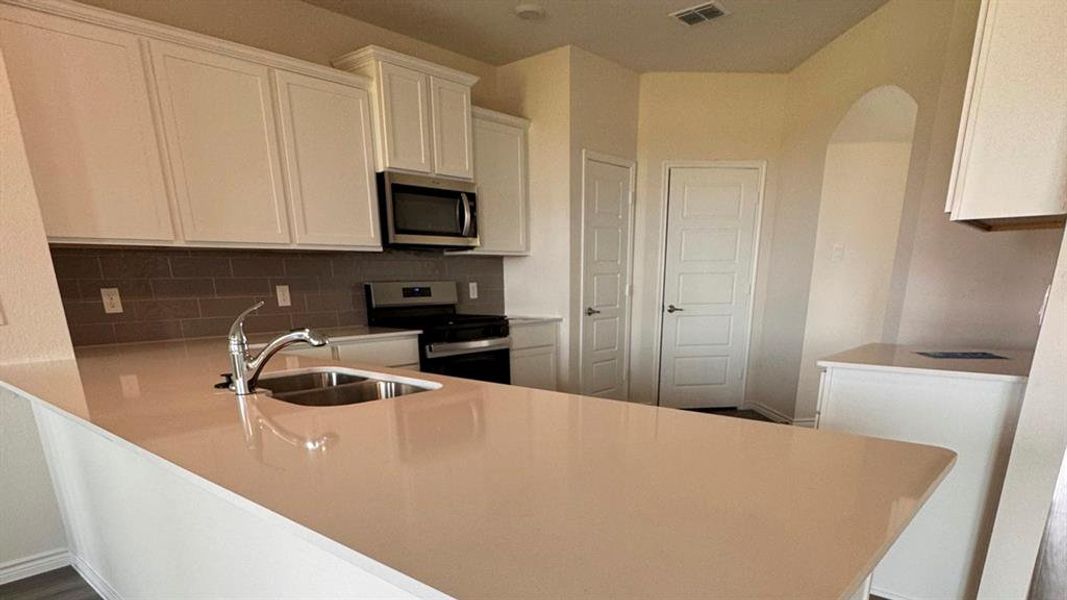 Kitchen featuring a peninsula, white cabinets, stainless steel appliances, and tasteful backsplash Kitchen featuring a peninsula, white cabinets, stainless steel appliances, and tasteful backsplash