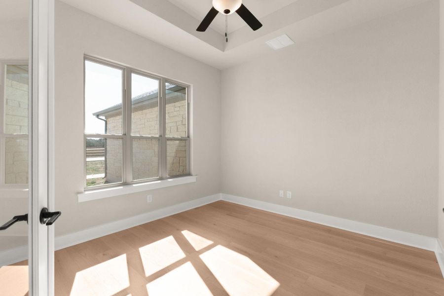 Empty room with light wood-type flooring, ceiling fan, and a tray ceiling