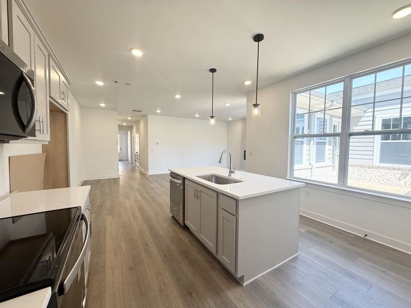 Kitchen featuring an island with sink, stainless steel appliances, dark wood-type flooring, decorative light fixtures, and light stone countertops