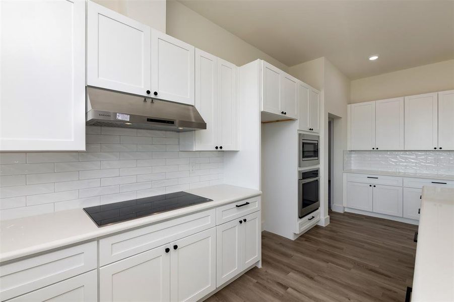Kitchen featuring white cabinetry, stainless steel appliances, under cabinet range hood, and wood finished floors