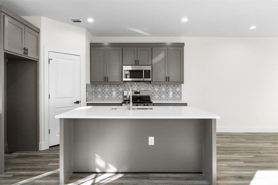 Kitchen featuring gray cabinets, stainless steel appliances, backsplash, dark wood-style floors, and light stone countertops Kitchen featuring gray cabinets, stainless steel appliances, backsplash, dark wood-style floors, and light stone countertops