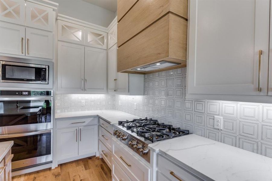 Kitchen featuring light hardwood / wood-style flooring, stainless steel appliances, white cabinets, and custom range hood