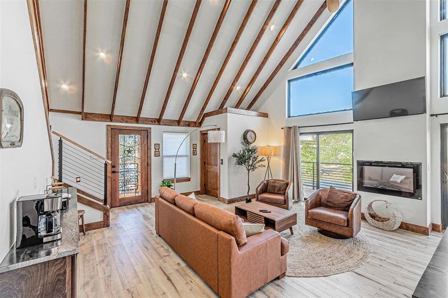 Living area with lofted ceiling, light wood finished floors, a glass covered fireplace, and recessed lighting