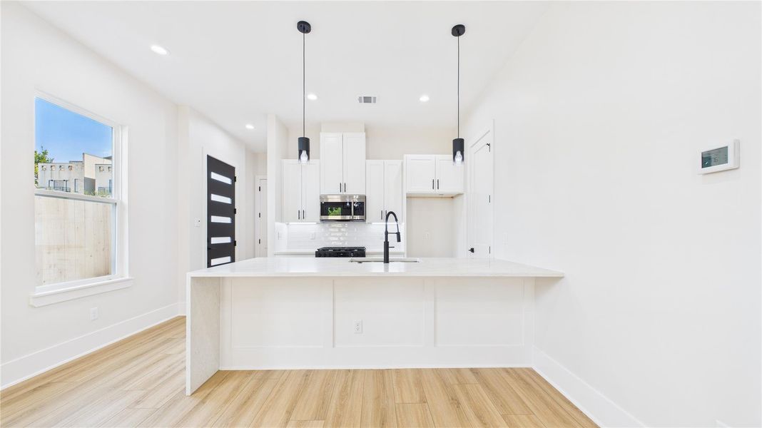 Bright and modern kitchen with a spacious open layout. Features white cabinetry, a large island with a sink, pendant lighting, and light wood flooring. Ideal for entertaining and cooking. Bright and modern kitchen with a spacious open layout. Features white cabinetry, a large island with a sink, pendant lighting, and light wood flooring. Ideal for entertaining and cooking.