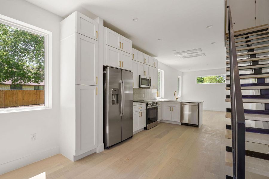 Kitchen with a sink, light wood-type flooring, a peninsula, white cabinetry, and stainless steel appliances