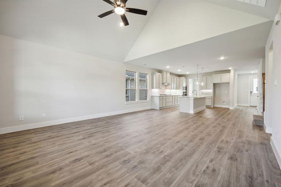 Unfurnished living room featuring hardwood / wood-style floors, ceiling fan, sink, and high vaulted ceiling