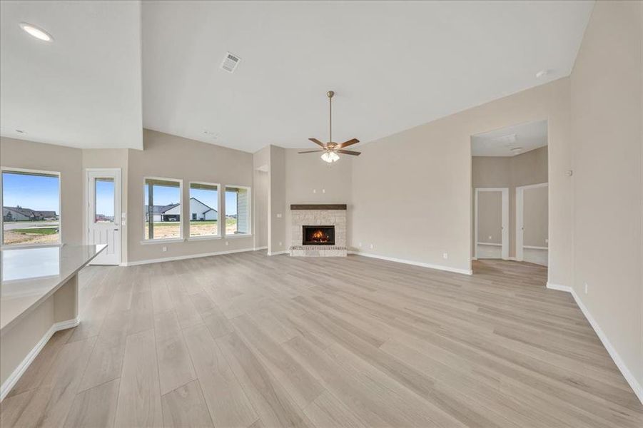 Unfurnished living room with light wood-style floors, ceiling fan, a lit fireplace, and high vaulted ceiling Unfurnished living room with light wood-style floors, ceiling fan, a lit fireplace, and high vaulted ceiling