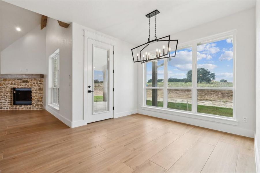 Unfurnished dining area featuring a fireplace, lofted ceiling with beams, light hardwood / wood-style flooring, and an inviting chandelier