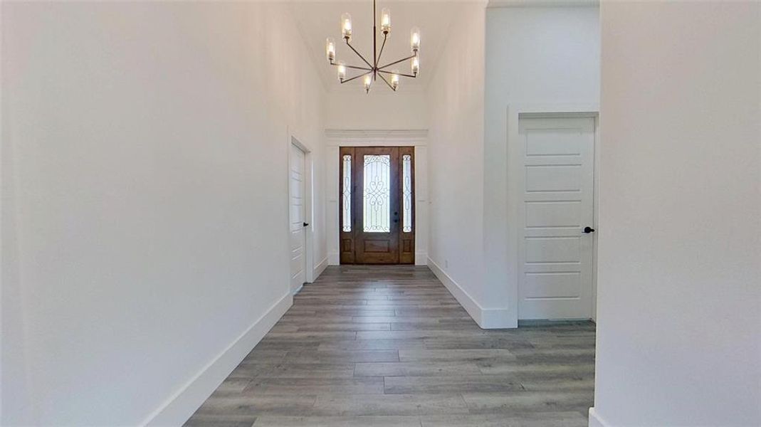 Foyer featuring a grand entrance door with decorative glass, vaulted ceiling, contemporary chandelier, and wood-finish flooring Foyer featuring a grand entrance door with decorative glass, vaulted ceiling, contemporary chandelier, and wood-finish flooring