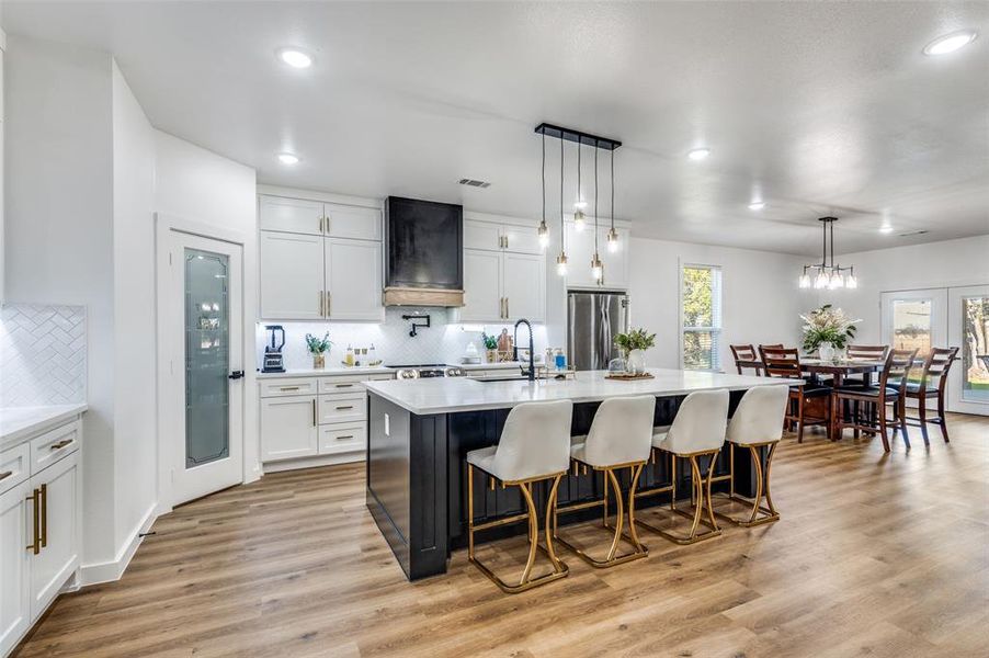Kitchen with a kitchen island with sink, decorative light fixtures, a kitchen breakfast bar, white cabinets, and recessed lighting