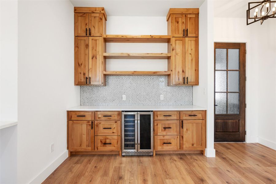 Indoor dry bar featuring wine cooler, light wood-type flooring, backsplash, and open shelves