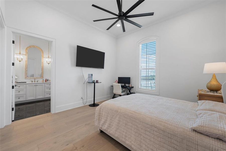 Bedroom with ornamental molding, light wood finished floors, ceiling fan, and ensuite bath