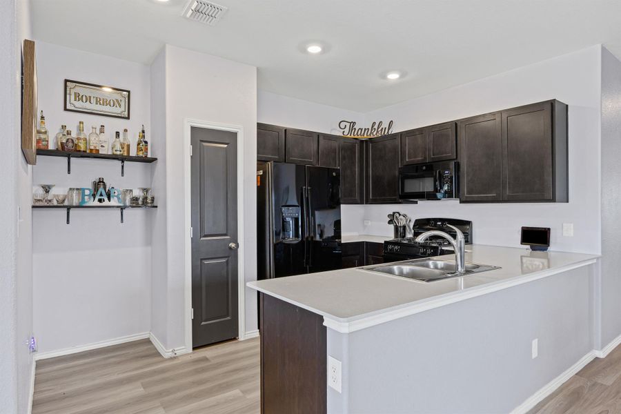 Kitchen with black appliances, a peninsula, light quartz countertops, LVP flooring, pantry, and dark brown cabinetry Kitchen with black appliances, a peninsula, light quartz countertops, LVP flooring, pantry, and dark brown cabinetry