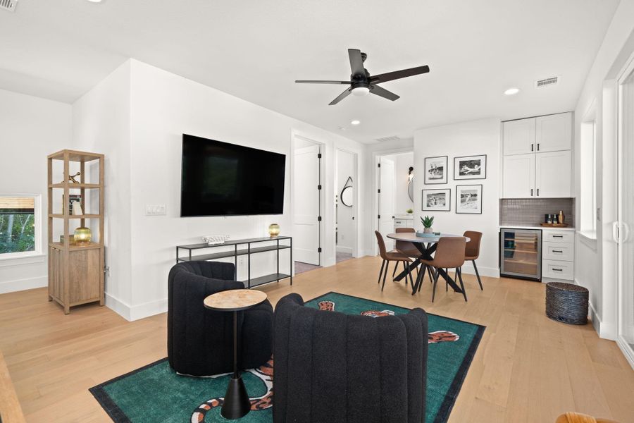 This modern living space features light wood flooring, a ceiling fan, and a sleek design. The kitchenette offers a mini-fridge and ample storage. Natural light fills the room, creating an inviting atmosphere.