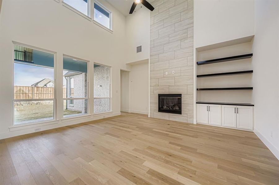 Unfurnished living room with light wood finished floors, a fireplace, a ceiling fan, and a towering ceiling