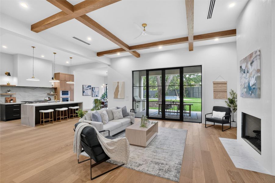 Exposed wood beams adorn the ceiling of this open-concept living space, illuminated by recessed lighting and a sleek ceiling fan.