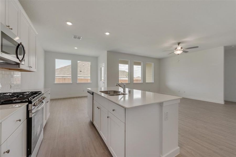 Kitchen featuring appliances with stainless steel finishes, tasteful backsplash, sink, a kitchen island with sink, and light wood-type flooring