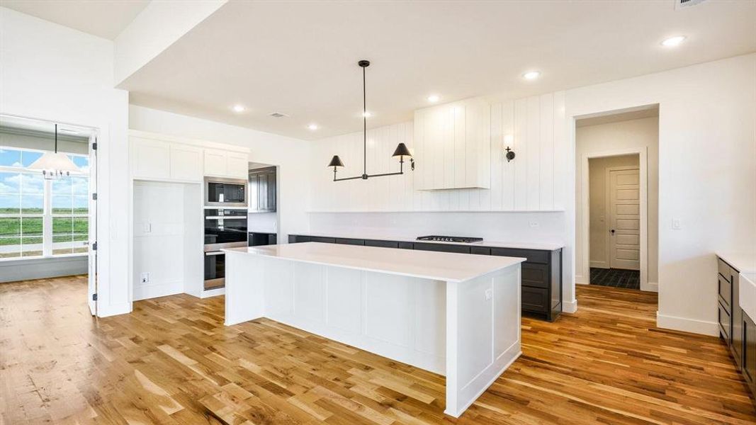 Kitchen with white cabinets, hanging light fixtures, built in microwave, light hardwood / wood-style flooring, and a center island