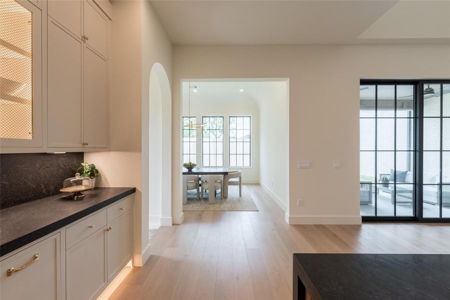 Framed by soft archways and rich black stone, the kitchen flows effortlessly into a dining room defined by its barrel-vaulted ceiling and custom 12-light grid windows. The visual symmetry and natural light create a serene transition between spaces, all grounded by warm European white oak floors and elevated by subtle curves throughout. Framed by soft archways and rich black stone, the kitchen flows effortlessly into a dining room defined by its barrel-vaulted ceiling and custom 12-light grid windows. The visual symmetry and natural light create a serene transition between spaces, all grounded by warm European white oak floors and elevated by subtle curves throughout.