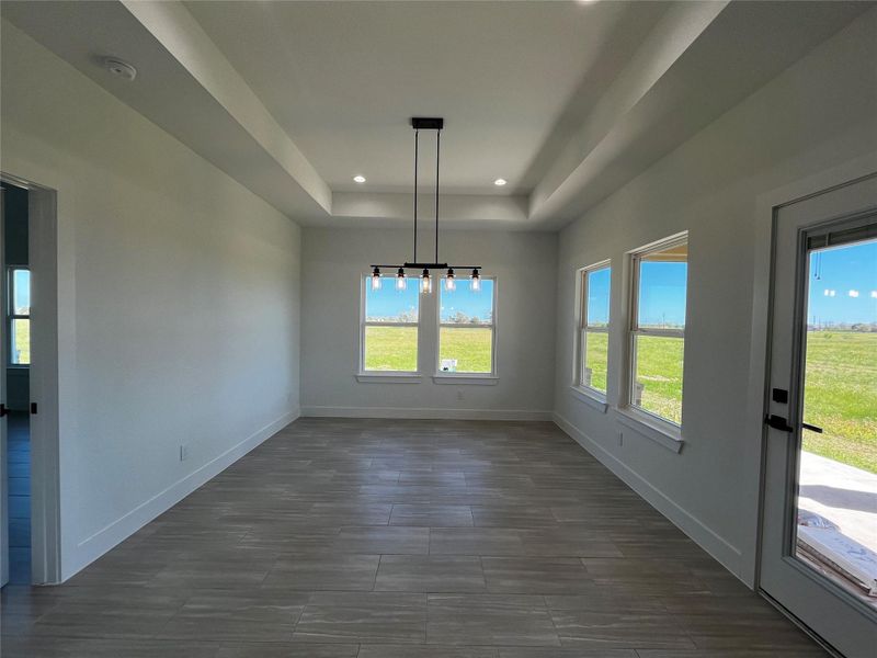 Bright and airy room with large windows and a modern light fixture, featuring tile flooring and views of a green landscape. Ideal for a dining area.