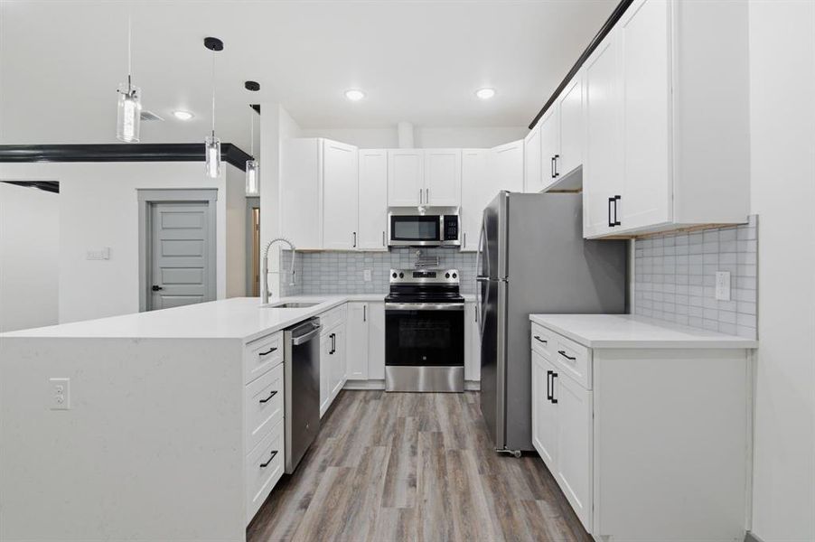 Modern kitchen featuring white cabinetry, stainless steel appliances, a spacious island with a sink, wood-finish flooring, and a subway tile backsplash