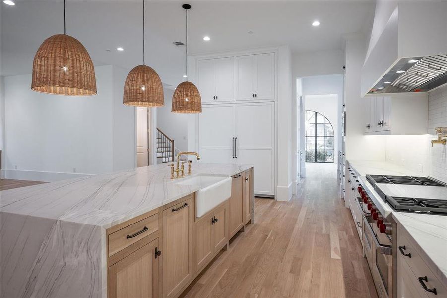 Kitchen with a center island with sink, premium range hood, double oven range, sink, and light wood-type flooring